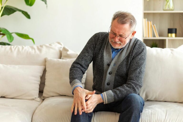 senior man suffering from joint ache or arthritis sitting on sofa at home.